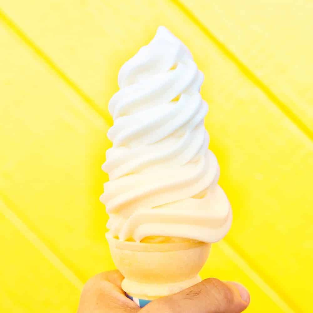 yellow background with white soft serve in a cone